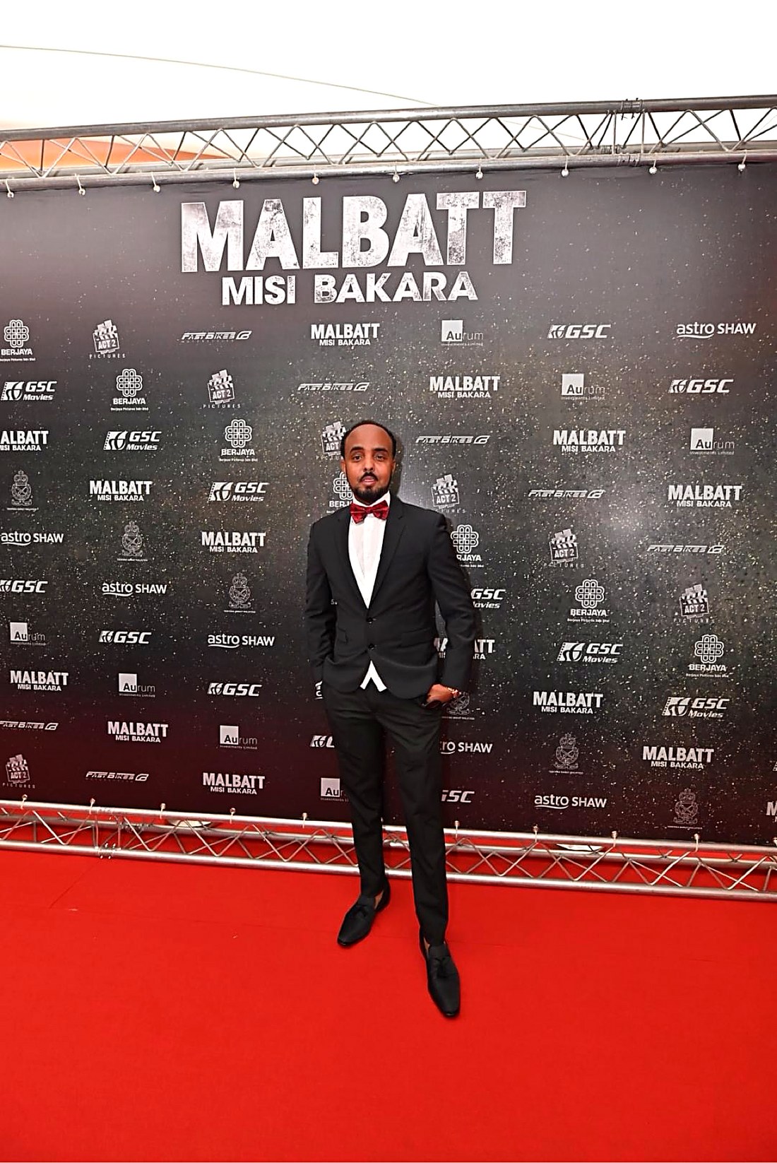 Musa Aden in a black tuxedo with a red bow tie on the red carpet at the Malbatt: Misi Bakara premiere